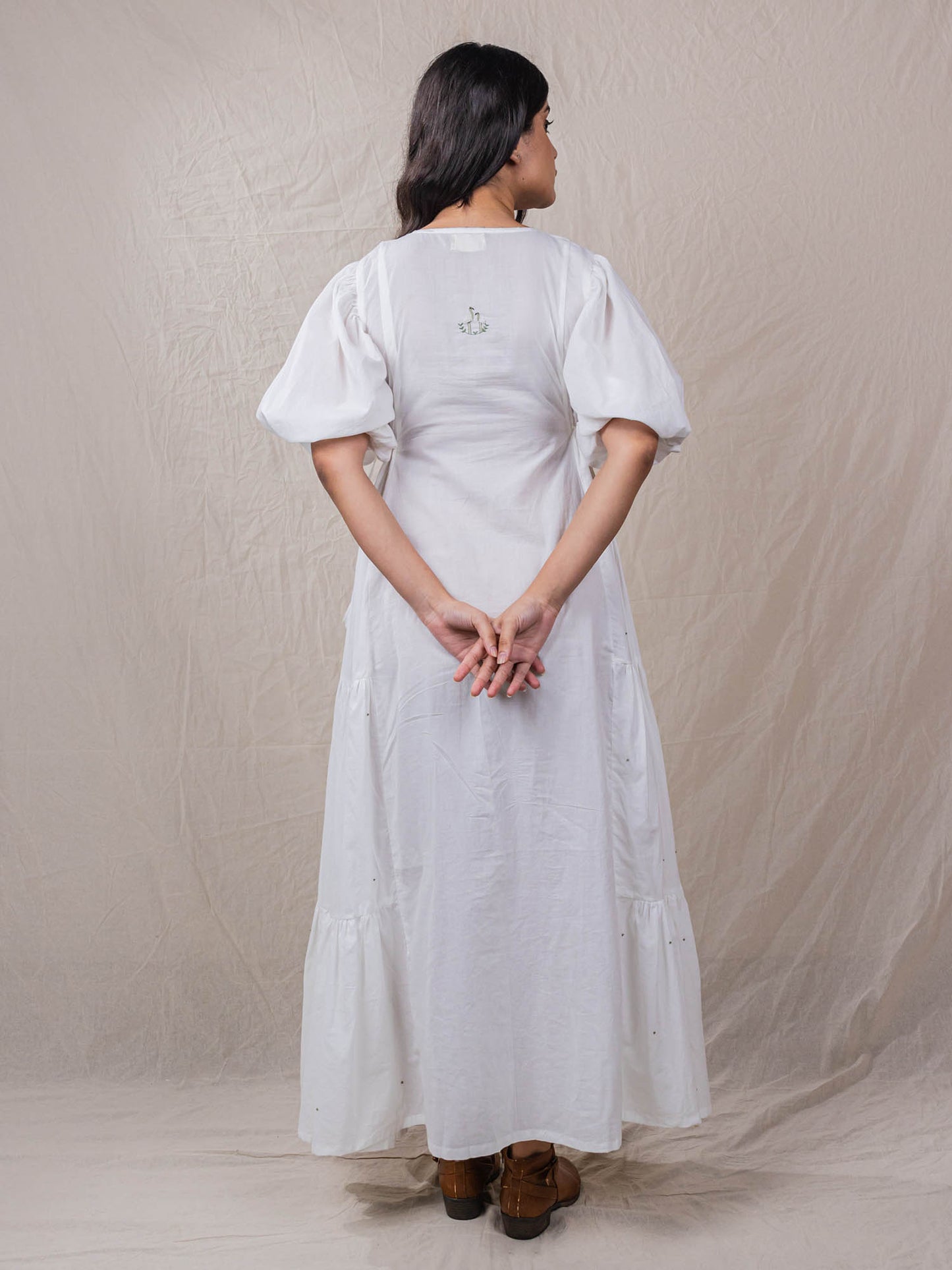 a line white colour dress in pure cotton. with tiers and gathers on the side. hand embroidered V neckline with other fine handwork details at the back of the dress.