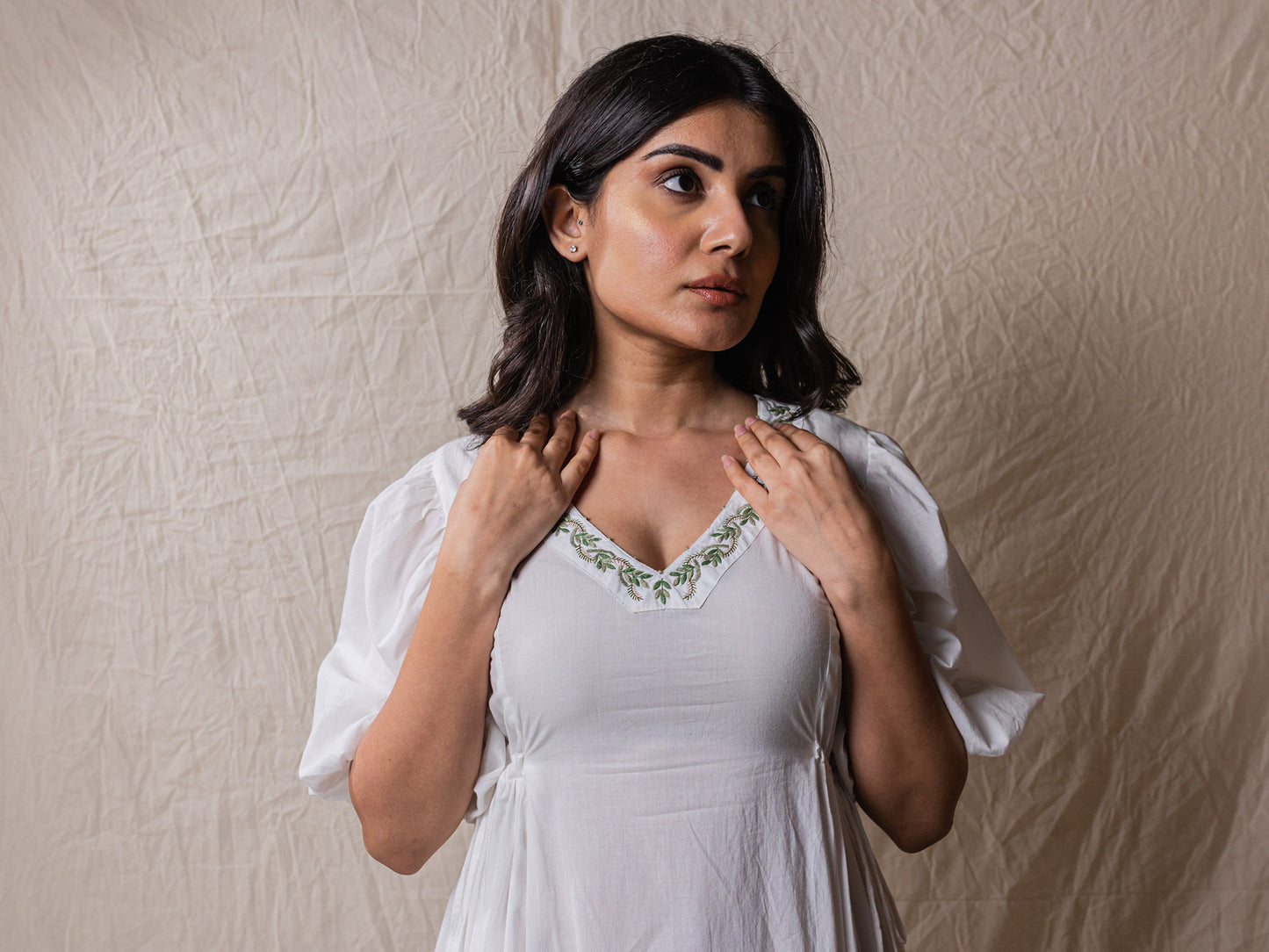 a line white colour dress in pure cotton. with tiers and gathers on the side. hand embroidered V neckline with other fine handwork details at the back of the dress.