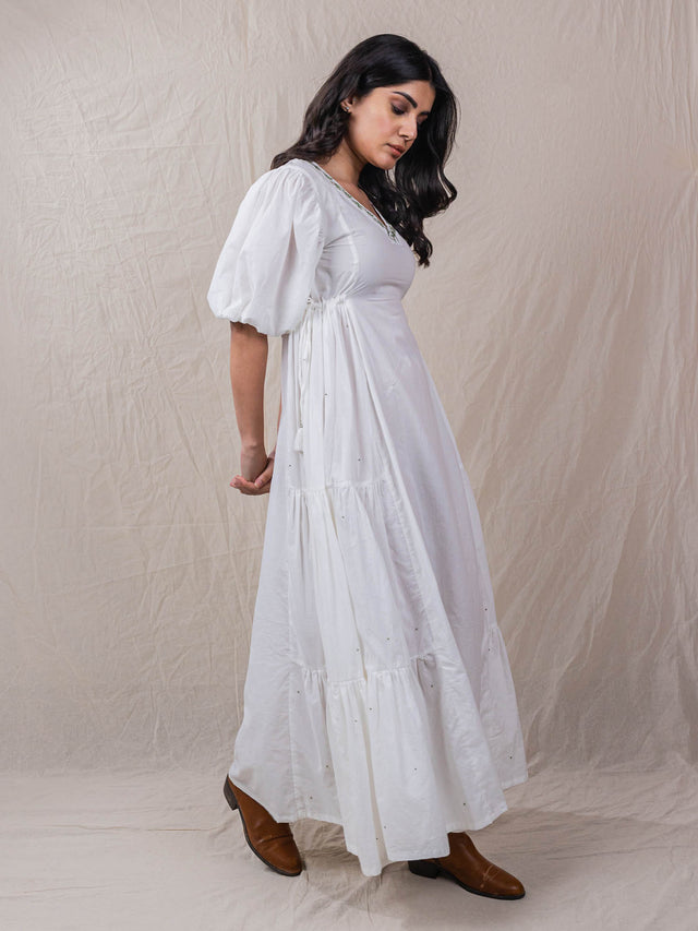 a line white colour dress in pure cotton. with tiers and gathers on the side. hand embroidered V neckline with other fine handwork details at the back of the dress.